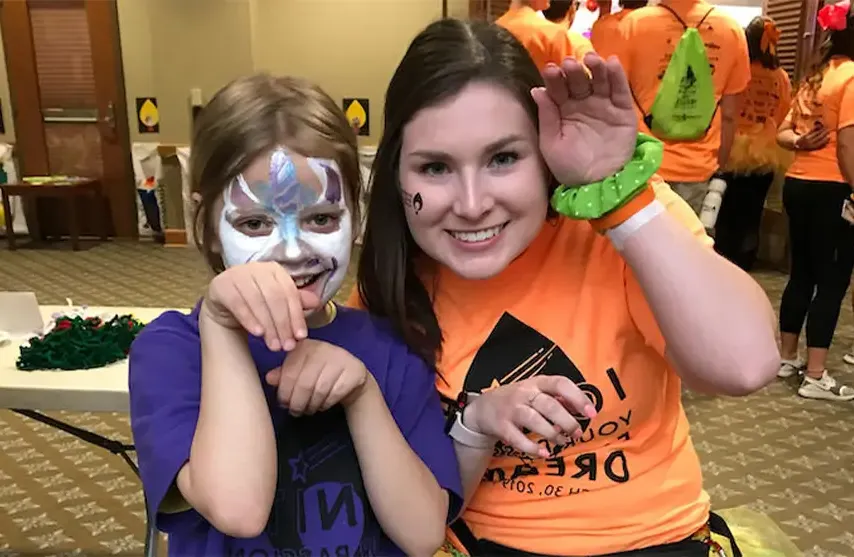 A smiling woman posing with a child with a painted face.