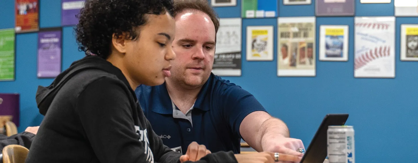 A student teacher pointing at a computer over the shoulder of a young student.